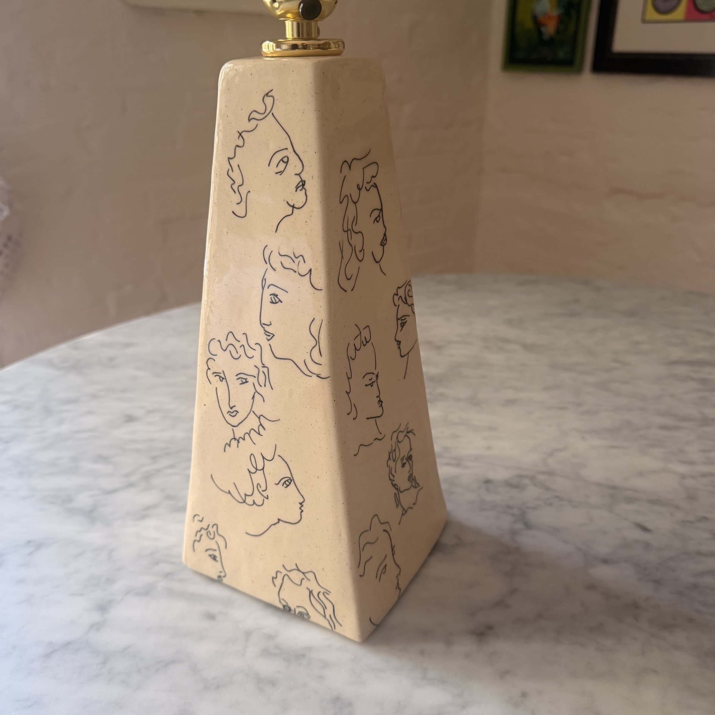 A pyramid-shaped ceramic lamp base covered in little painted faces.