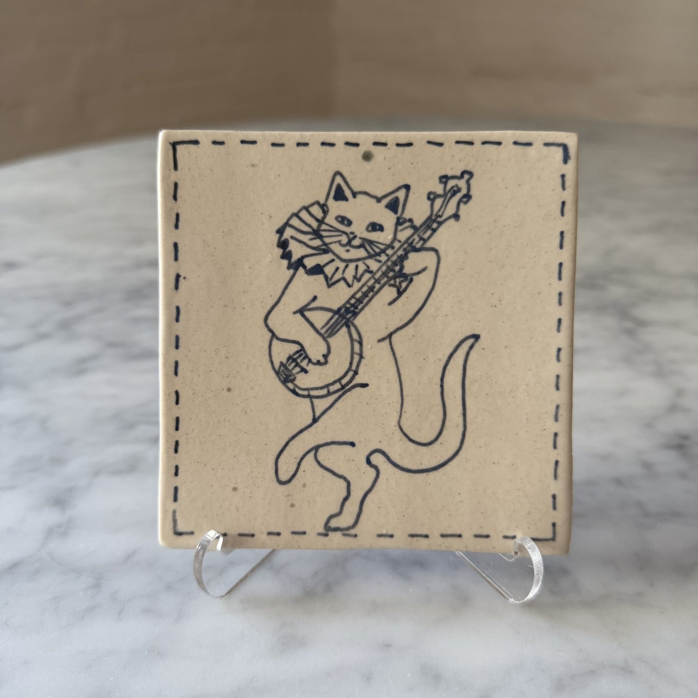 A hand-painted tile of a cat playing a lute.