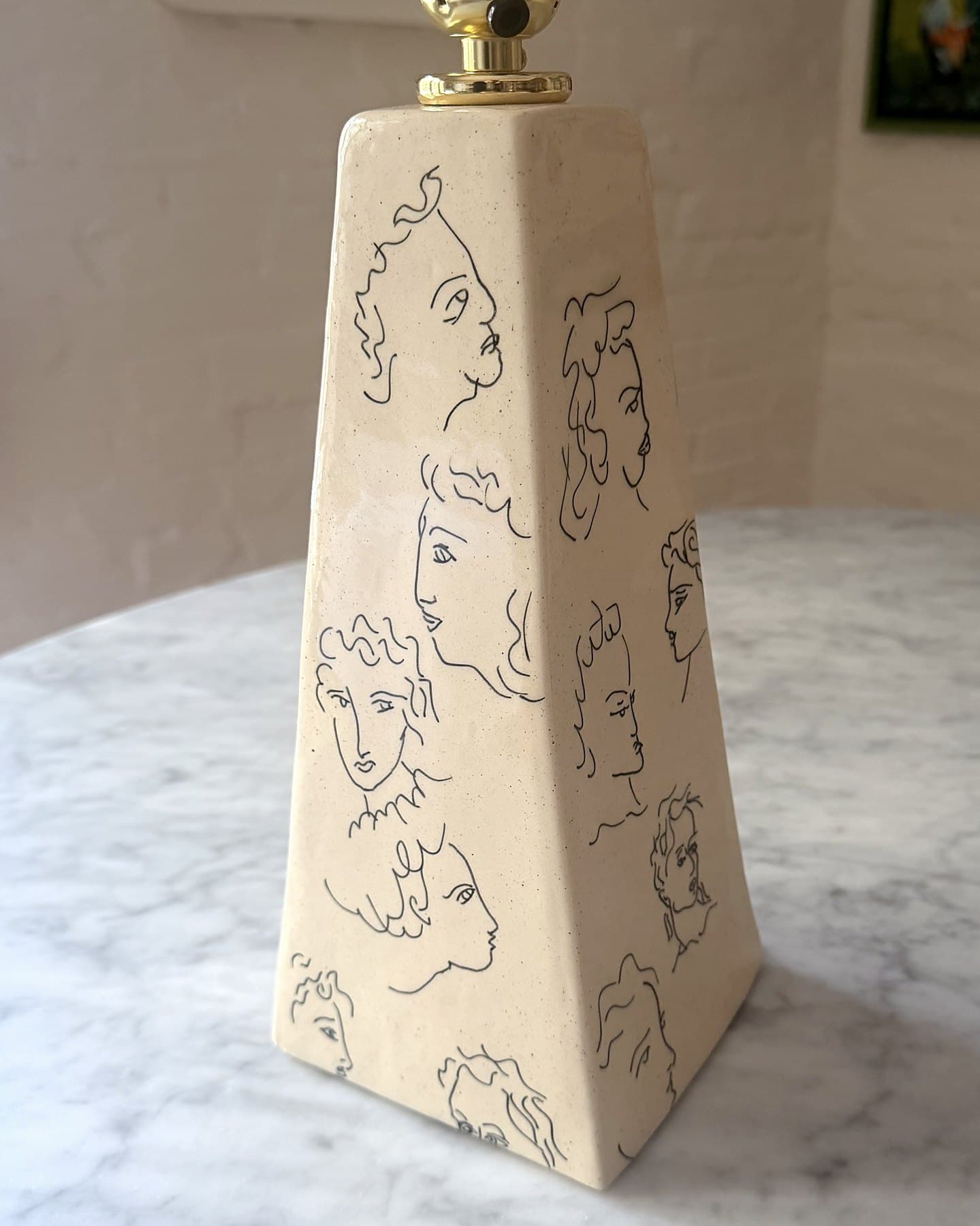 A tall, tapered ceramic lamp base covered in line-drawn faces, with a brass socket.