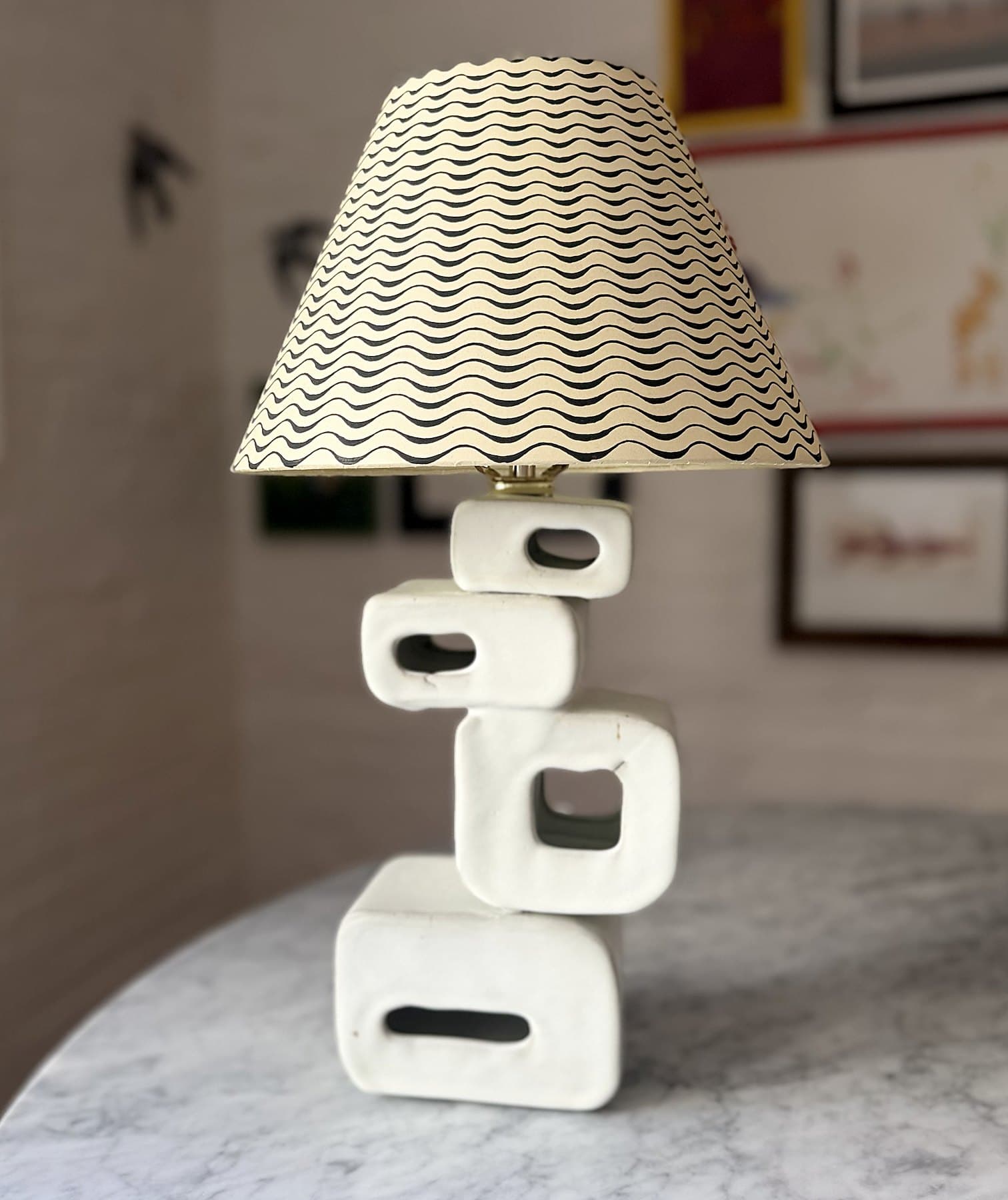 A lamp with a base of four stacked, pierced white ceramic blocks and a cream shade printed with black waves.
