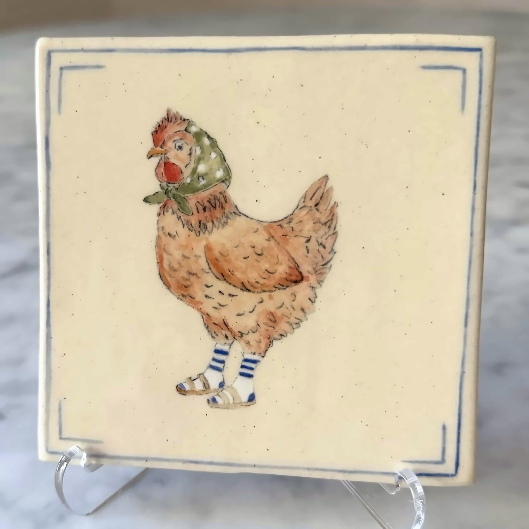 A tile painted with a hen in a polka-dot headscarf, striped socks and sandals.