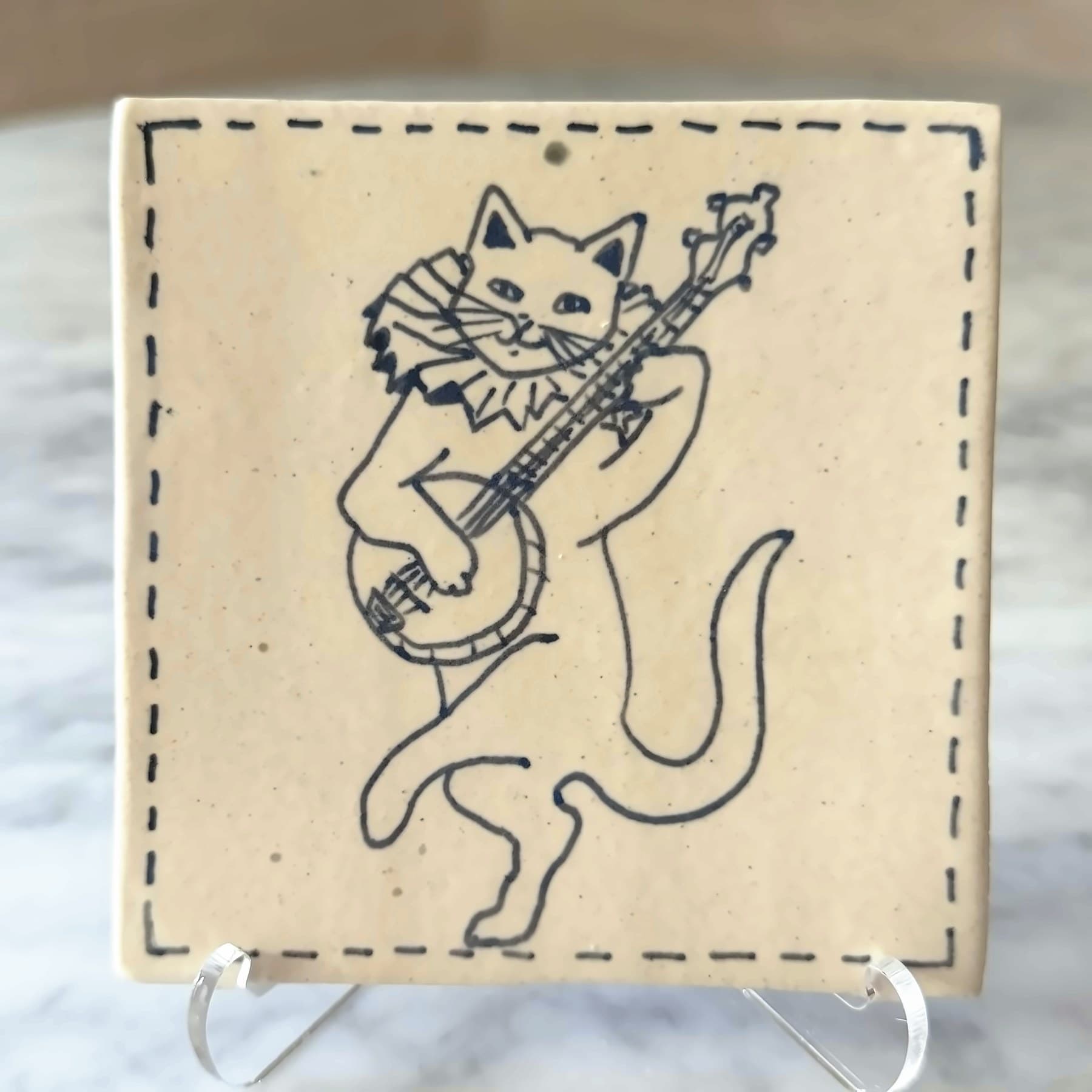 A tile drawn in blue line with a dancing cat in a ruffled collar playing the banjo.