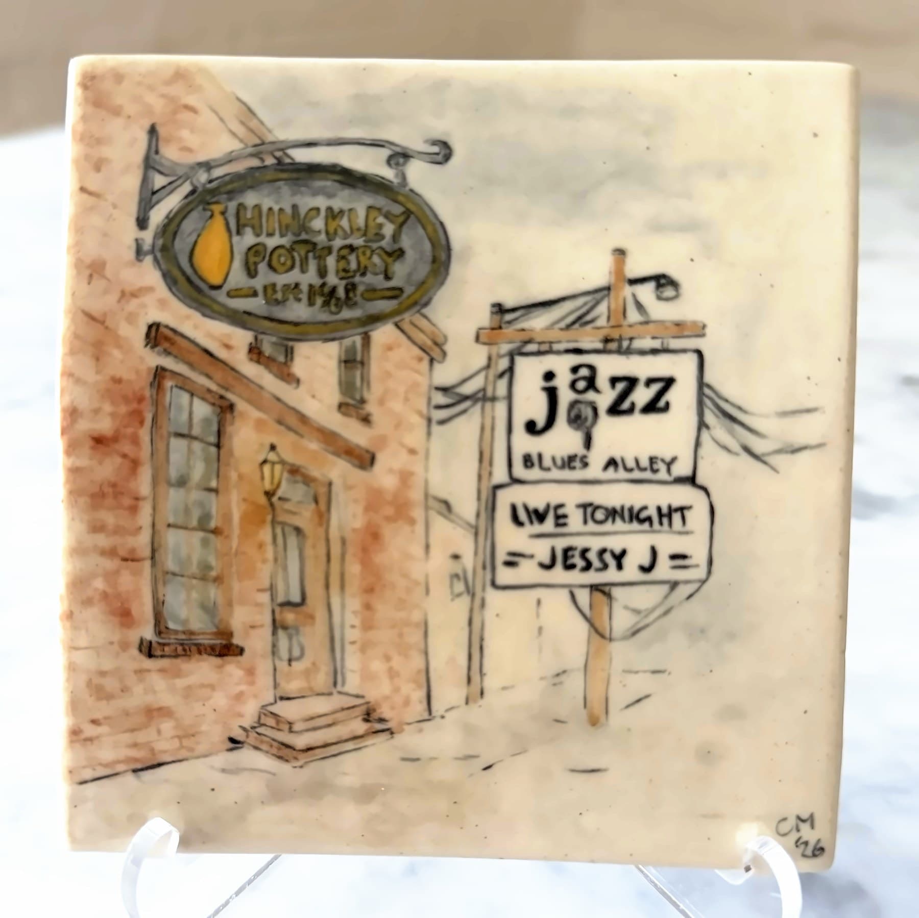 A tile painted with a Georgetown alley: the Hinckley Pottery sign on a brick building and a Blues Alley jazz sign.