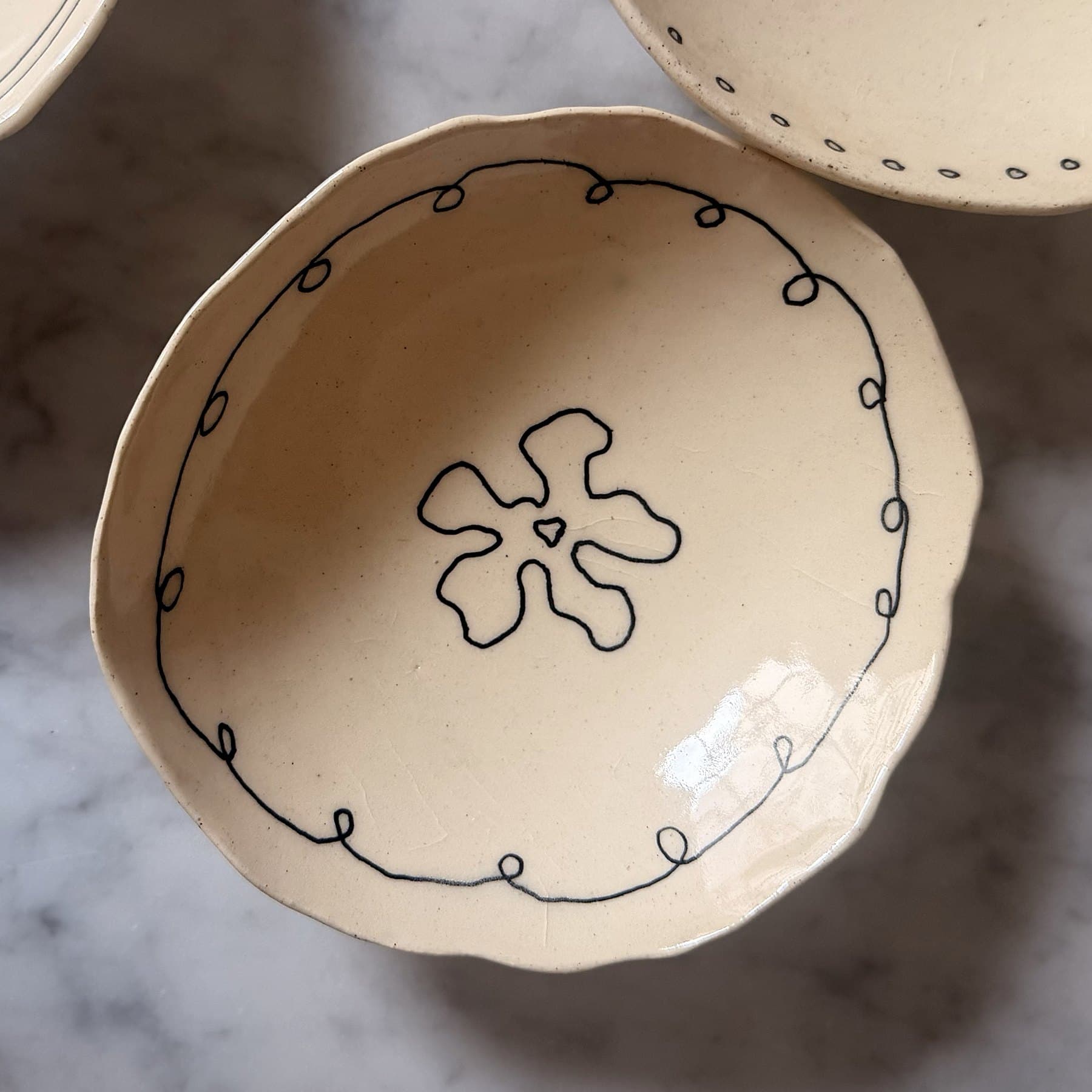 A hand-built cream bowl with a looped black border and one large flower.