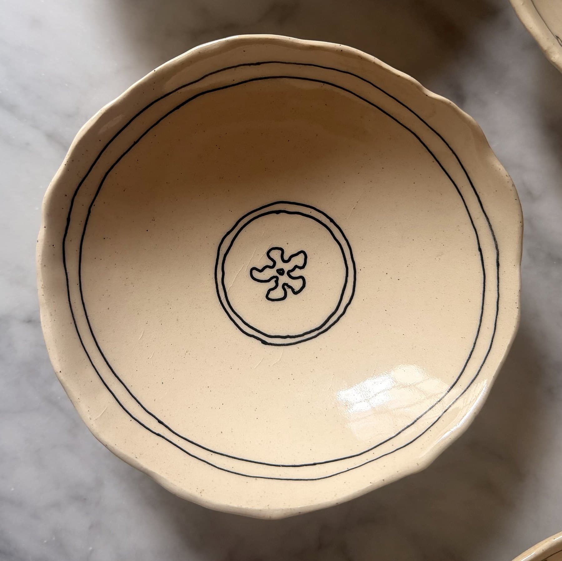 A scalloped cream bowl with a double-line border and a small flower in a circle.